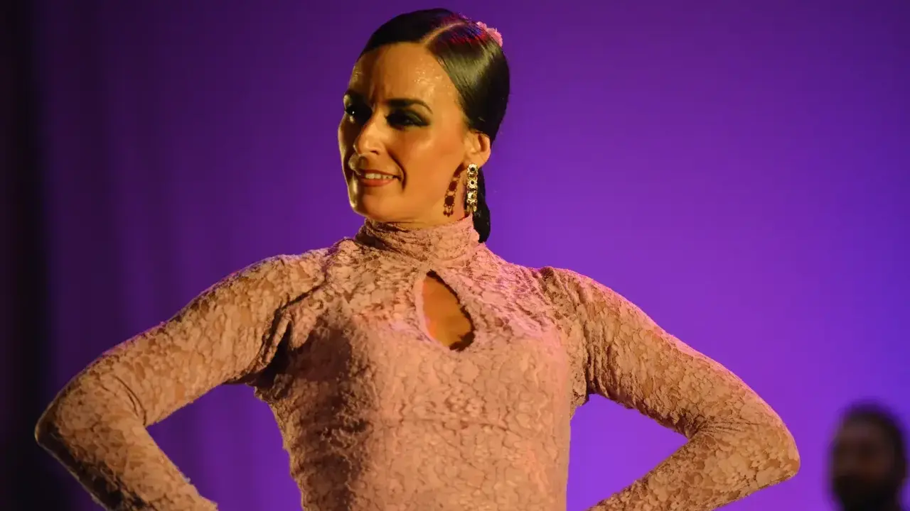 Bailaora de flamenco, con un vestido de encaje rosa, interpreta una seguiriya con pasión bajo luces púrpuras.