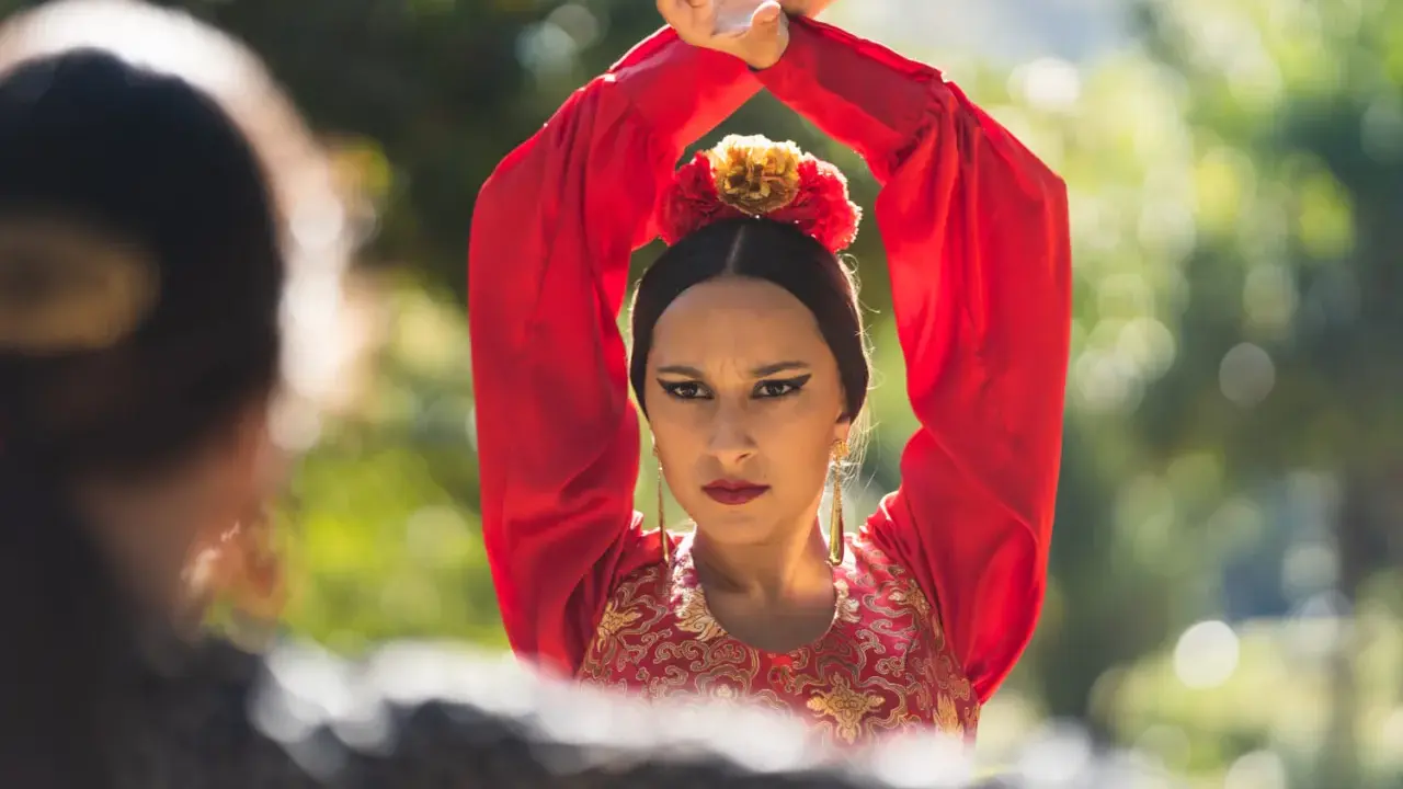 Mujer con traje rojo de flamenca, brazos en alto, mirando a otra persona.