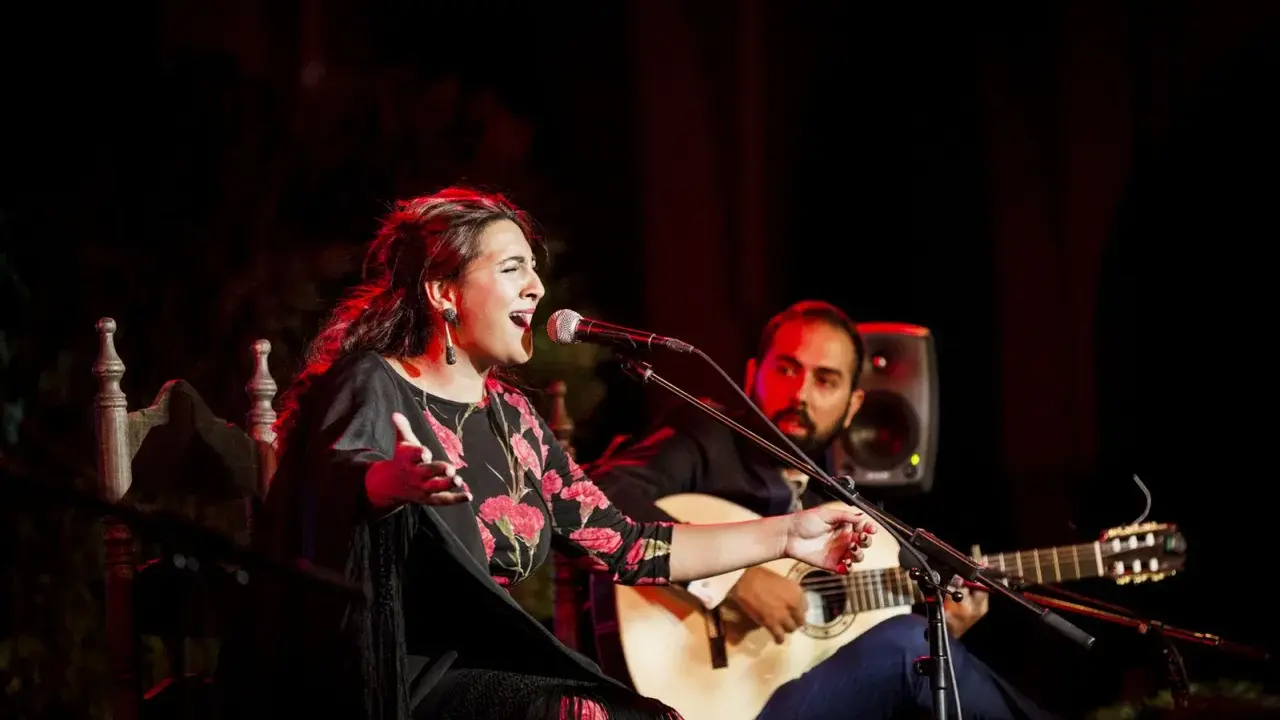 Cantante de flamenco actual, con vestido floral, canta apasionadamente mientras un guitarrista la acompaña.