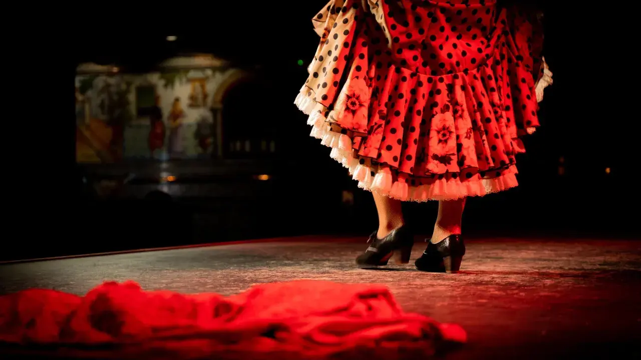 Pies de bailaora con volantes de lunares y flores, listos para un apasionado baile por bulerías.