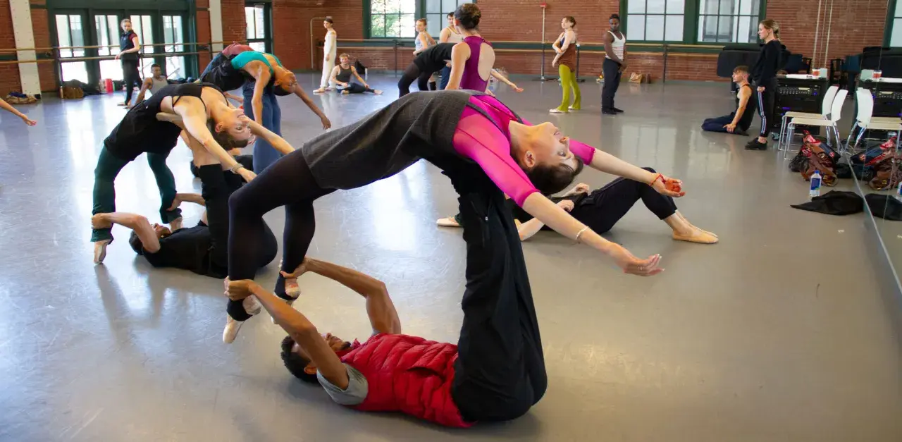 Un grupo de bailarines practica una coreografía compleja, con un hombre en el suelo sosteniendo a una mujer en el aire, evocando la pasión de un flamenco.