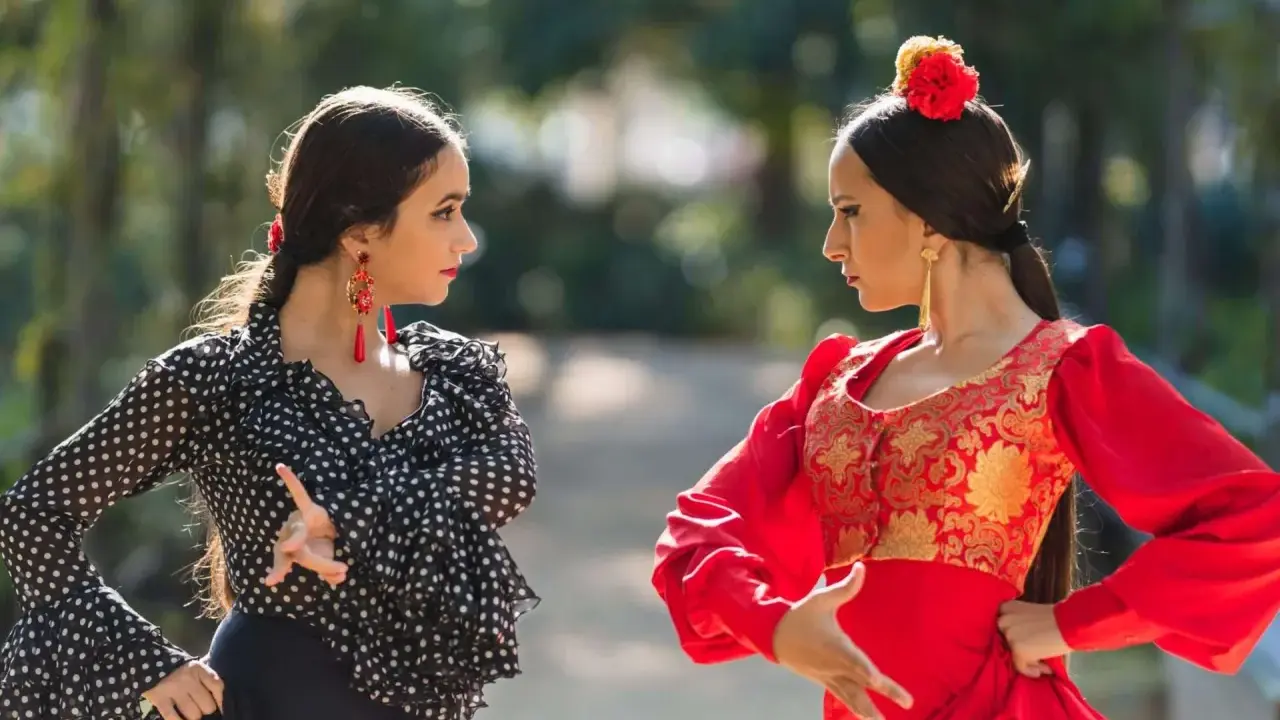 Dos mujeres practican baile flamenco para principiantes en un parque, una con traje de lunares y otra de rojo vibrante.
