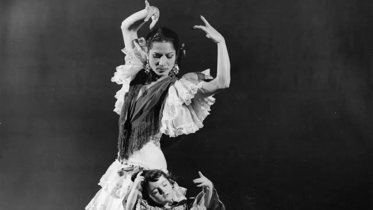 Una bailarina española famosa, con volantes y mantón, baila con gracia mientras una niña yace a sus pies.