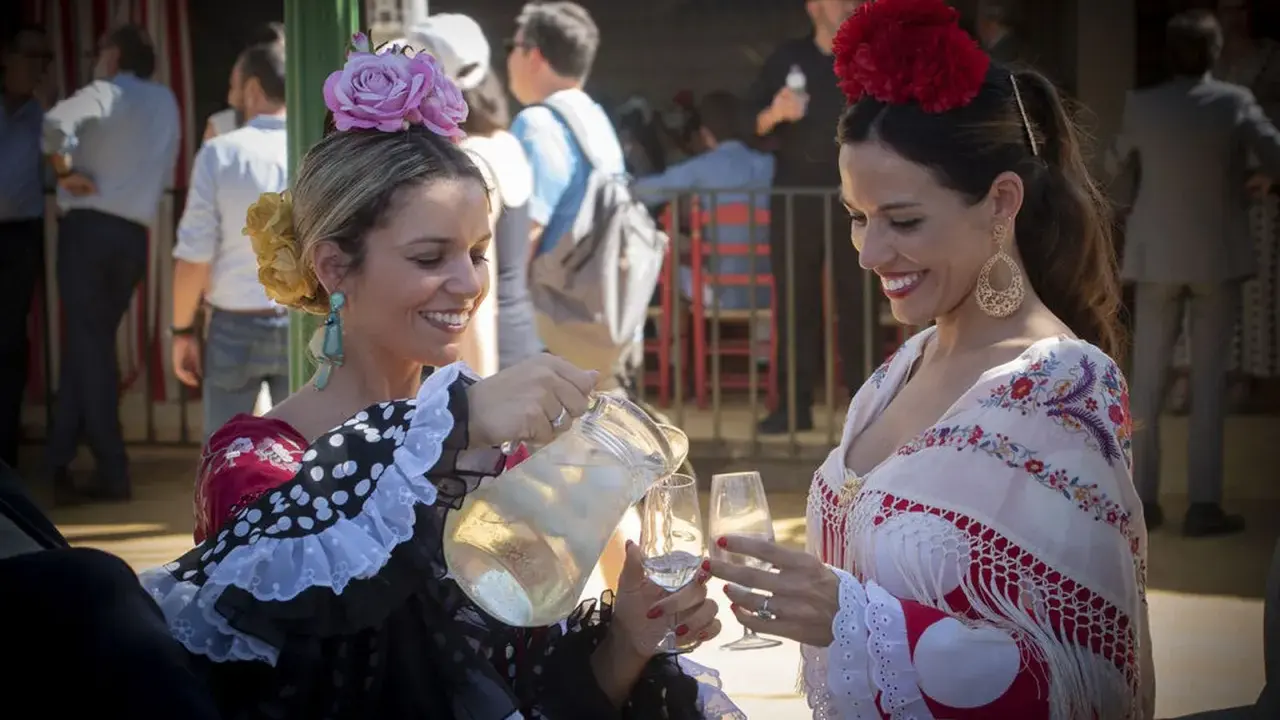 Dos mujeres con trajes de flamenca, una sirviendo bebida. Un vistazo a la historia del traje de flamenca.