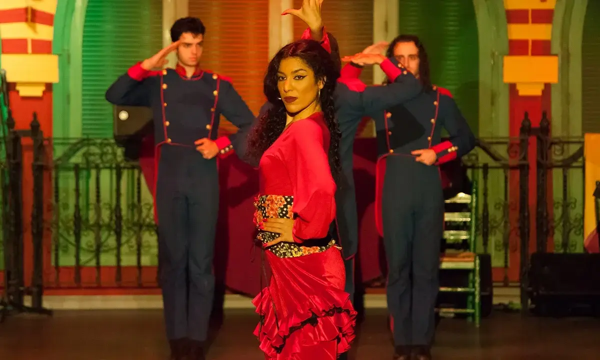 Una bailaora de flamenco con un vestido rojo vibrante, rodeada por dos hombres con uniformes militares, capturando la esencia de las alegrías flamenco.