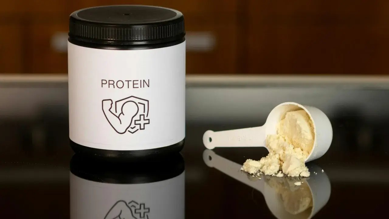 Un bote de proteína y una cuchara con polvo. Ideal para saber como tomar proteína y potenciar tus entrenamientos.
