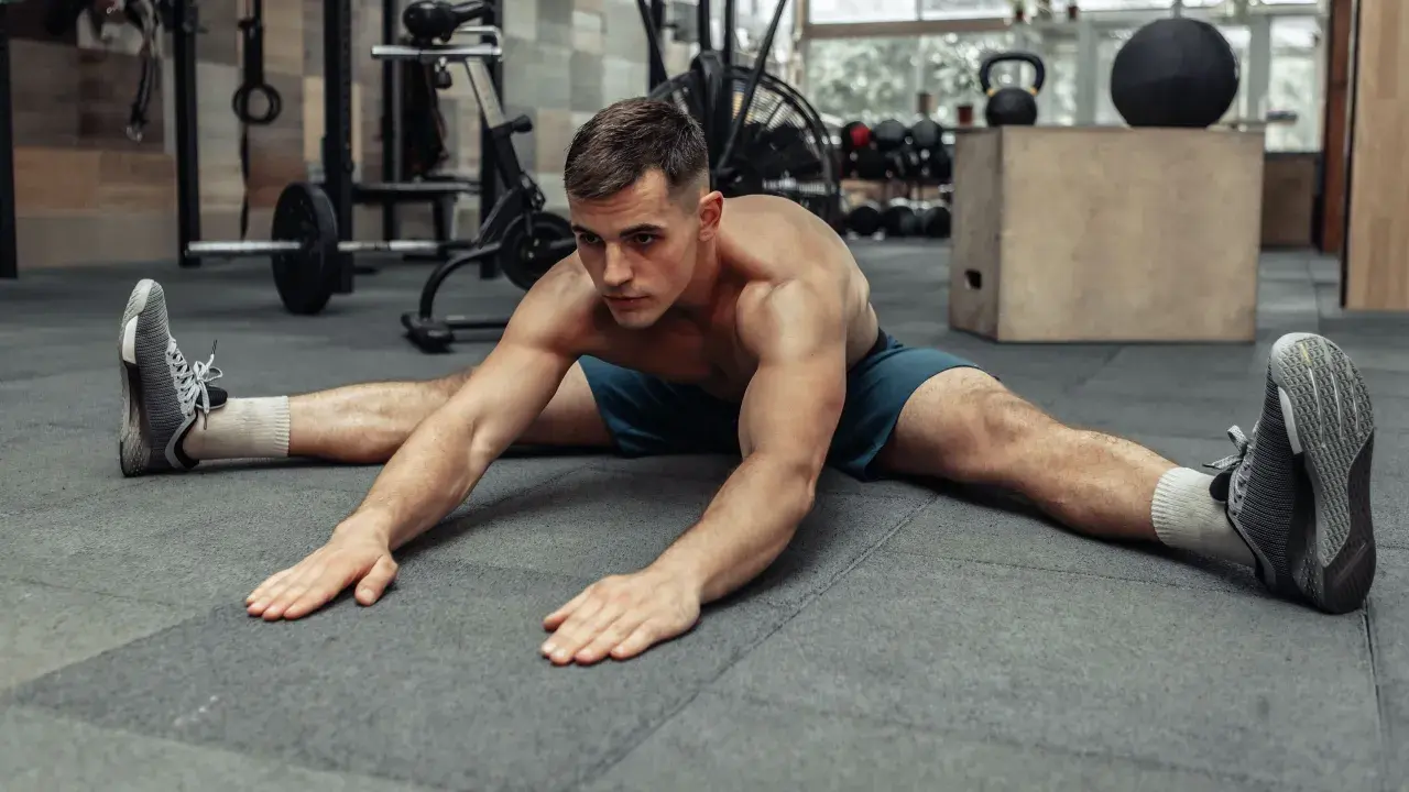Hombre haciendo estiramiento de piernas en el suelo, preparándose para el calentamiento antes de entrenar.