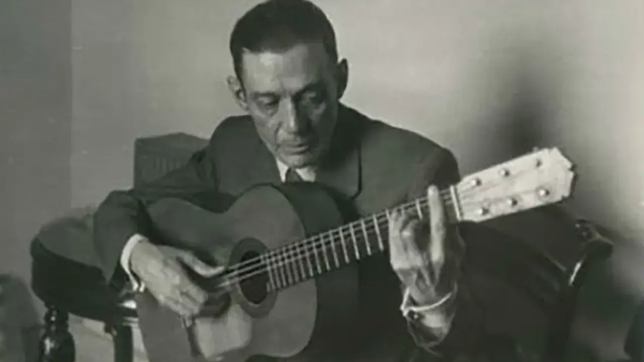 Un guitarrista flamenco andaluz, con traje y corbata, toca su guitarra con pasión.