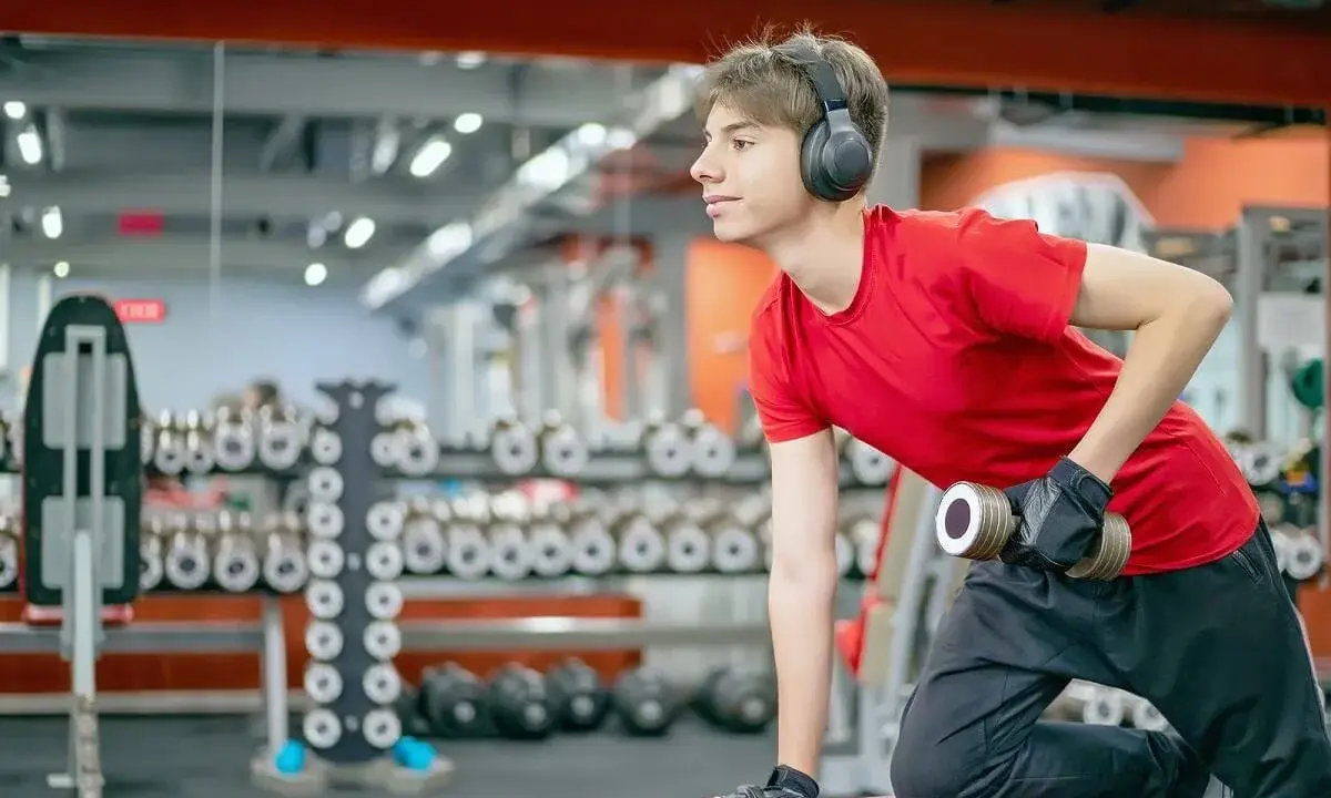 Joven con auriculares entrena en gimnasio. ¿Hacer pesas a los 15 años detiene mi crecimiento?