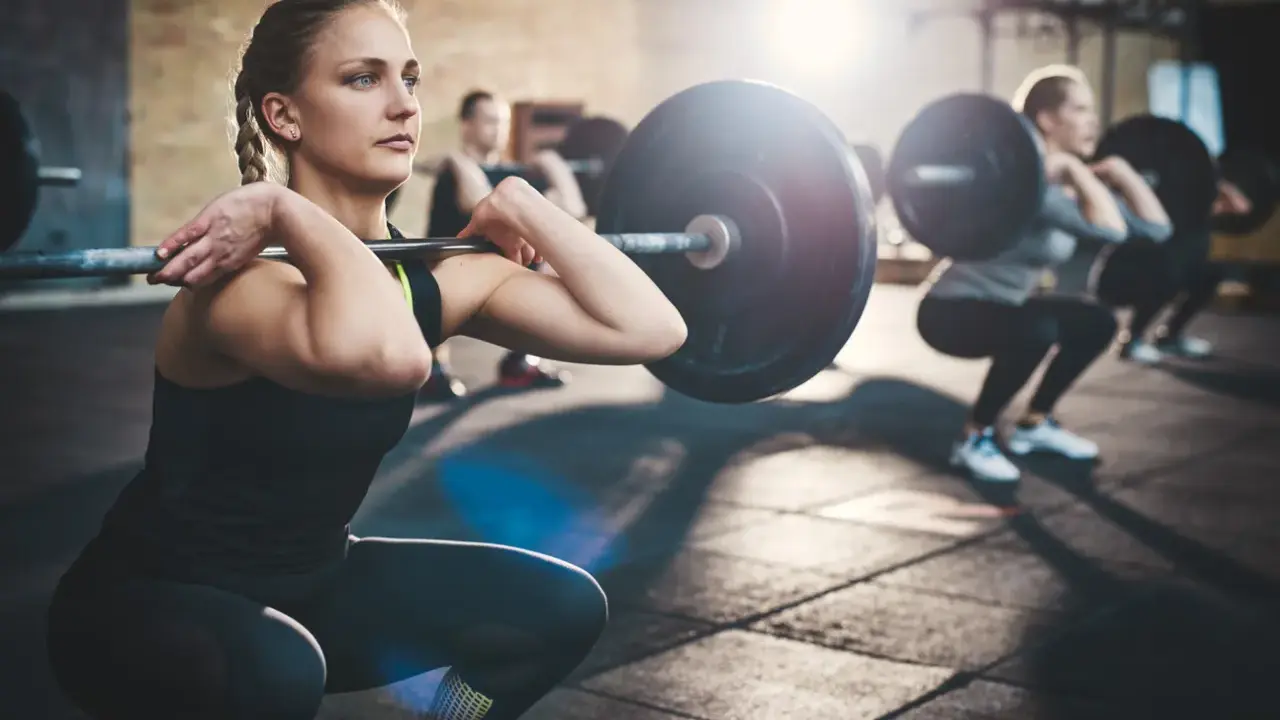 Mujeres realizando sentadillas con barra, un ejemplo de ejercicios compuestos en el gym.