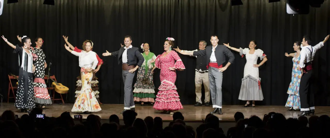 Artistas de sevillanas y flamenco en escena, con trajes coloridos y movimientos apasionados.