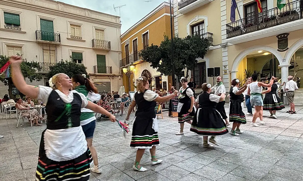 Un grupo de mujeres realiza un animado fandango dance en una plaza, vestidas con trajes tradicionales.