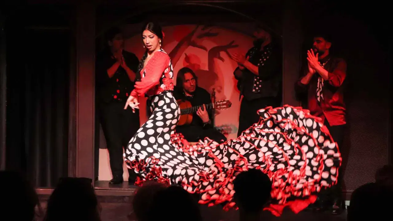 Bailarina flamenca con vestido de lunares, guitarrista y palmas. El sonido flamenco llena el ambiente.