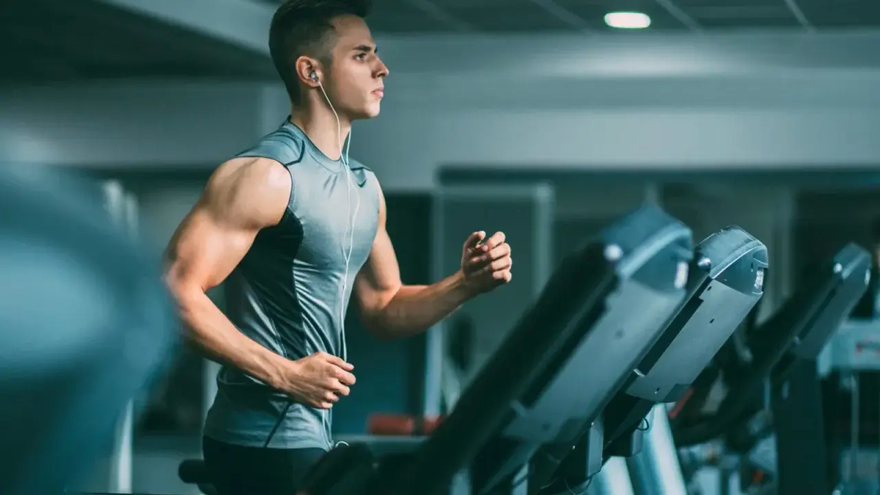 Joven con audífonos haciendo liss cardio en una cinta de correr en el gimnasio.