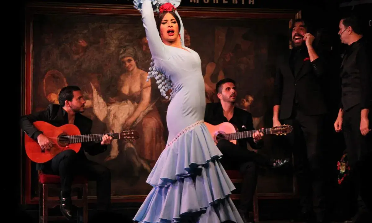 Una bailaora deslumbra con su traje azul, rodeada de guitarristas y cantantes, en una actuación que evoca a las mejores bailaoras de flamenco actuales.