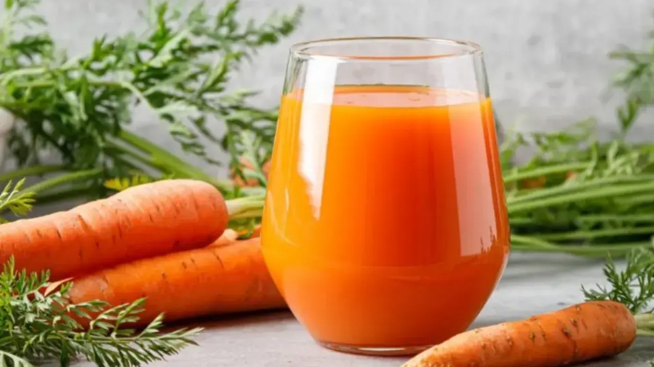 Un vaso de jugo de zanahoria fresco junto a zanahorias enteras. Descubre para qué es buena la zanahoria: ¡salud y vitalidad!