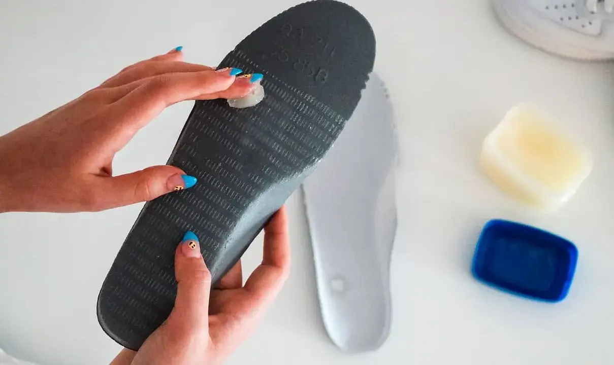 Manos aplicando vaselina en una plantilla para zapatos, un método para como quitar ruido zapatos goma.