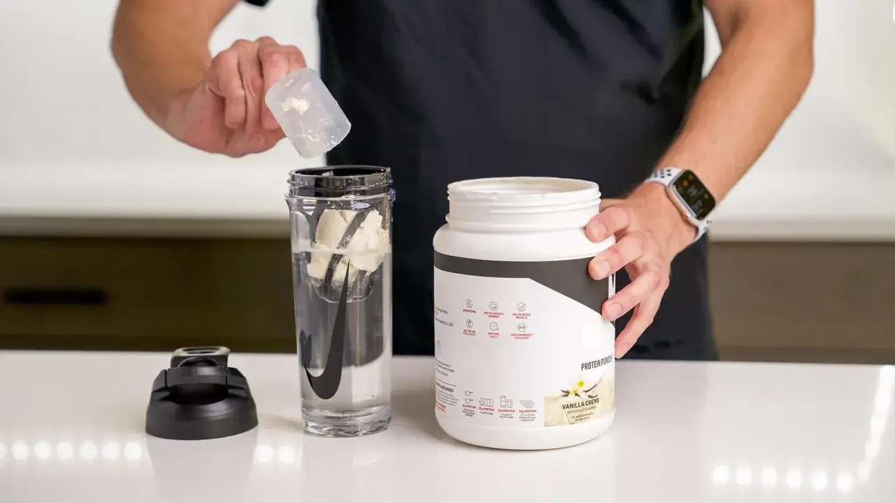 Hombre prepara batido con proteína en polvo para ganar músculo. El envase indica para qué sirve la proteína en polvo: energizar y recuperación post-entreno.