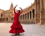 Una sevillana flamenca baila con pasión frente a un edificio histórico.