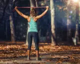 Mujer entrenando tren superior con tabla de ejercicios y gomas elásticas en un parque otoñal.