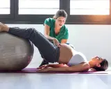 Entrenadora ayuda a una embarazada a hacer ejercicios con pelota en el gym.