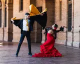 Pareja bailando flamenco con pasión. Él, con capa negra y dorada, ella, con vestido rojo voluminoso. Un jaleo flamenco lleno de arte.