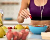 Mujer en ropa deportiva prepara su desayuno saludable con frutas frescas, pensando en qué desayunar antes de entrenar.