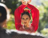 Mujer con traje rojo de flamenca, brazos en alto, mirando a otra persona.