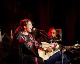 Cantante de flamenco actual, con vestido floral, canta apasionadamente mientras un guitarrista la acompaña.