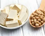 Tofu cortado en cubos en un bol blanco y una cuchara de madera llena de semillas de soja. ¿A qué sabe el tofu?