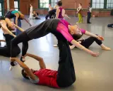Un grupo de bailarines practica una coreografía compleja, con un hombre en el suelo sosteniendo a una mujer en el aire, evocando la pasión de un flamenco.