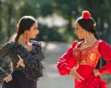 Dos mujeres practican baile flamenco para principiantes en un parque, una con traje de lunares y otra de rojo vibrante.