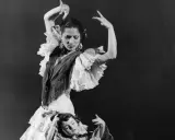 Una bailarina española famosa, con volantes y mantón, baila con gracia mientras una niña yace a sus pies.