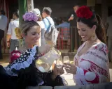 Dos mujeres con trajes de flamenca, una sirviendo bebida. Un vistazo a la historia del traje de flamenca.