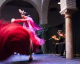 Una bailaora española gira con su vestido rojo, creando un torbellino de tela. A su lado, un guitarrista acompaña con su música.