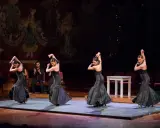 Cuatro bailarinas de flamenco, vestidas de negro, ejecutan pasos apasionados. Un percusionista las acompaña.