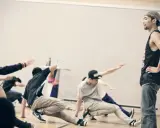 Jóvenes practicando una coreografía de break dance, con movimientos en el suelo y un instructor observando.
