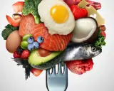 Un tenedor carga una variedad de alimentos saludables, incluyendo salmón, aguacate, huevo, bayas y verduras bajas en carbohidratos, ideal para una dieta equilibrada.