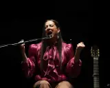 Cantante flamenco mujer, con el alma desbordada, canta apasionadamente frente al micrófono. A su lado, una guitarra espera.