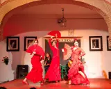 Tres bailarinas de flamenco, vestidas de rojo y con abanicos, ejecutan fandangos flamencos en un escenario.