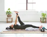 Mujer haciendo el ejercicio "dead bug" en una alfombra, estirando una pierna hacia arriba.