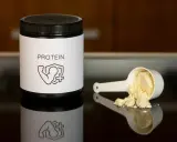 Un bote de proteína y una cuchara con polvo. Ideal para saber como tomar proteína y potenciar tus entrenamientos.