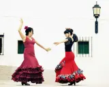 Dos mujeres con trajes vibrantes ejecutan apasionados bailes flamencos frente a una pared blanca.
