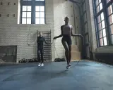 Dos mujeres realizan ejercicios de calentamiento general saltando la cuerda en un gimnasio industrial.
