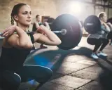 Mujeres realizando sentadillas con barra, un ejemplo de ejercicios compuestos en el gym.