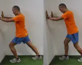 Hombre realizando estiramientos después de correr contra una pared, apoyando las manos y extendiendo una pierna hacia atrás para estirar el gemelo.
