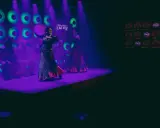 Dos bailarinas de danza sevillana, con trajes vibrantes, actúan bajo luces púrpuras y verdes.
