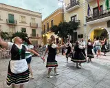 Un grupo de mujeres realiza un animado fandango dance en una plaza, vestidas con trajes tradicionales.