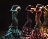 Cuatro mujeres flamencas bailando con vestidos de volantes en tonos tierra.