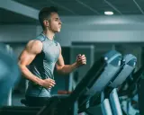 Joven con audífonos haciendo liss cardio en una cinta de correr en el gimnasio.